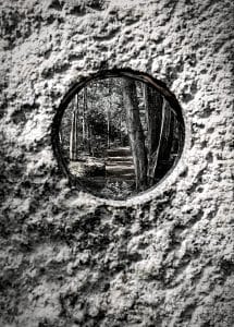 This thought-provoking photograph, titled "Concrete Path," is artfully captured at the Coastal Maine Botanical Gardens in Boothbay, Maine. The image cleverly employs a concrete aperture to frame a crisply focused forest scene along the garden's trail, illustrating a striking contrast between the rough, blurred texture of the concrete and the detailed natural environment. This composition underscores the juxtaposition of man-made structures with the untouched beauty of nature, inviting viewers to reflect on the interplay between built environments and natural landscapes.