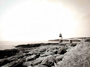 This photograph. Taken on 07/17/2024, captures the Marshall Point Lighthouse, famously known as the "Forrest Gump Lighthouse" due to its appearance in the movie "Forrest Gump." Located in Port Clyde, Maine, the lighthouse stands at the end of a picturesque white wooden walkway extending over rugged coastal rocks. The image is rendered with a vintage, artistic effect, enhancing the lighthouse's historical charm and the dramatic coastal landscape. The soft pastel sky adds a serene, timeless quality to the scene, making it a captivating subject for photography enthusiasts and admirers of maritime history.