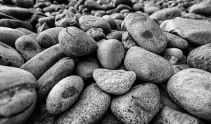 A close-up black and white photograph capturing the smooth, rounded rocks at Little Hunters Beach in Acadia National Park. The image emphasizes the varied textures and shapes of the stones, creating a detailed and contemplative coastal scene.