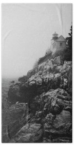 Bass Harbor Lighthouse shrouded in fog, perched on rugged cliffs, with a monochrome palette.