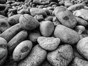 Black and white photograph of smooth, weathered rocks on a beach, captured by Blaine Stoner.