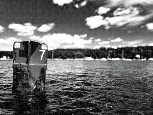 Black and white photograph of a buoy marked "7" floating in the bay, with the shoreline and sky in the background, captured by Blaine Stoner.