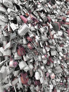 Photograph of a dense collection of love locks with a selective color effect highlighting the reds against a metallic gray background, captured by Blaine Stoner.