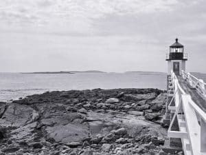 Marshall Point Lighthouse stands proudly overlooking the rugged shores of Port Clyde, Maine. This photograph captures the iconic scene of the lighthouse, known for its long wooden walkway extending out towards the open waters. With the distant islands on the horizon and rocky coastline in the foreground, this image evokes a sense of tranquility and timeless beauty. The Marshall Point Lighthouse has served as a guiding light since 1832, and remains a symbol of the area's maritime history. Blaine Stoner’s black-and-white composition adds a dramatic, nostalgic feel, perfectly framing the lighthouse in its natural surroundings.