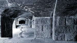 A photograph of the cannon hallway at Fort Knox in Bucksport, Maine, featuring sturdy brick arches and stone walls, creating a sense of depth and historical significance. The cool tones and strong lines of the architecture evoke the fort's role in military history.