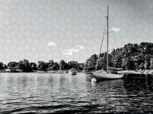 Black and white photograph of sailboats moored in a calm harbor with a tree-lined shoreline, captured by Blaine Stoner.