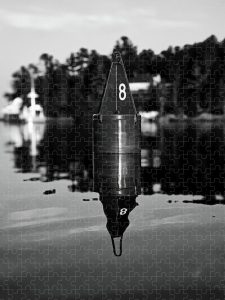 No. 8 Buoy Puzzle by Blaine Stoner featuring a black-and-white image of a buoy with the number 8 reflected in calm waters.