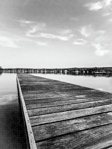 The Dock Puzzle by Blaine Stoner featuring a solitary dock extending into calm waters in black-and-white tones.