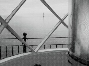 Black and white photograph of the view from Breakwater Lighthouse in Rockland, Maine, focusing on a distant sailboat framed by the lighthouse's windows, captured by Blaine Stoner.