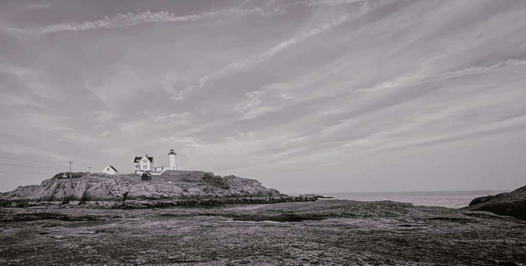 Standing resilient against sea and time, Nubble Lighthouse rises from its rocky perch off the coast of York, Maine—an enduring symbol of New England’s maritime soul. Captured in rich monochrome, this image invites viewers to experience the drama and solitude of the coast, where jagged granite meets a sky in motion. The stark contrast between the weathered foreground and the iconic tower draws the eye inward, emphasizing both the power of nature and the quiet strength of the lighthouse itself. Every detail—from the cloud-streaked sky to the solid geometry of the structure—echoes the permanence and poise of this historic landmark. This photograph is a tribute to coastal Maine’s untamed beauty and the timeless presence of Nubble Light as it keeps its watch from the rock.