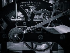 A close-up view of the E. Howard & Co. clock mechanism in the Blue Hill Baptist Church belfry, capturing its intricate gears and levers in striking black and white detail.