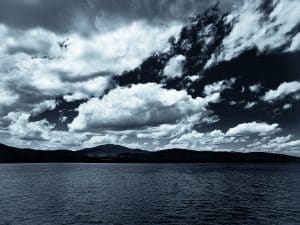 A dramatic black-and-white view of Moosehead Lake in Greenville, Maine, beneath a vast, cloud-filled sky.