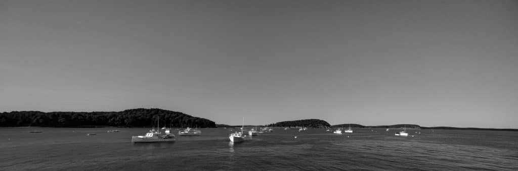 Black and white photograph of boats anchored in Bar Harbor, Maine, with the Porcupine Islands in the distance.