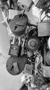 Black and white close-up photograph of the Lock Wall, featuring padlocks inscribed with names and dates, attached to a fence in Portland, Maine.